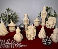 a group of white candles sitting on top of a red cloth covered table next to christmas decorations