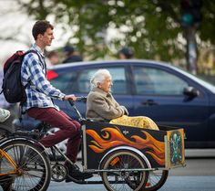 an old man riding on the back of a bike with a woman in it