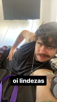 a man laying on top of a bed next to a purple bag and a flat screen tv