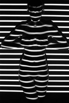 a black and white photo of a woman with stripes on her body in front of a striped wall