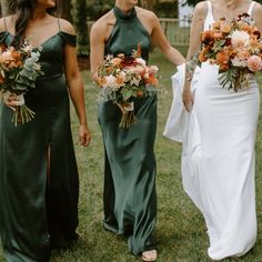 three bridesmaids in green dresses holding bouquets and smiling at each other on the grass