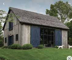 two horses are standing in front of a barn with blue shutters and large windows