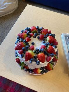 a cake with strawberries and blueberries is on a table next to a book