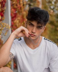 a young man sitting on the ground wearing a white shirt and silver chain around his neck