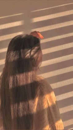 a woman standing in front of a window with blinds on her face and long hair