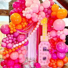 there are many balloons and streamers on the wall in front of this house that is pink, orange, and white