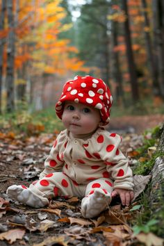 a baby wearing a red and white polka dot hat sitting on the ground in leaves