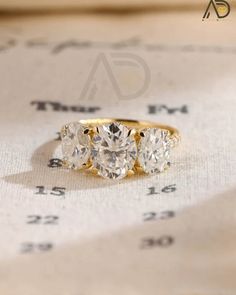 three stone diamond ring sitting on top of a piece of paper with numbers in the background