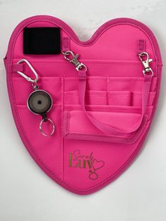 a pink heart shaped purse with keychains and clippings attached to it