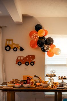 a table topped with lots of desserts and balloons in the shape of trucks on top of it