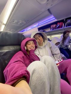 two people sitting on an airplane and one is wearing a pink outfit while the other wears a white hat