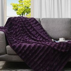 a couch with a purple blanket on top of it and a coffee cup in the middle