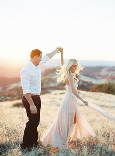 a man and woman dancing in a field at sunset with the sun shining on them