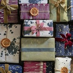 many wrapped presents are stacked on top of each other with ribbons and orange slices tied to them