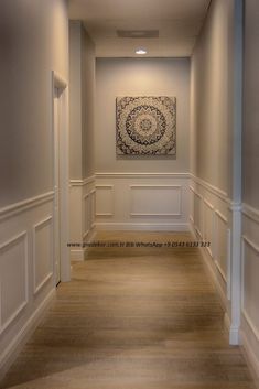 an empty hallway with white walls and wood flooring is pictured in this image, there is a painting on the wall