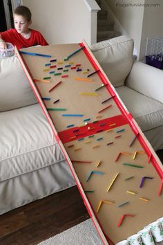 a young boy sitting on a couch in front of a cardboard box with colored sticks sticking out of it