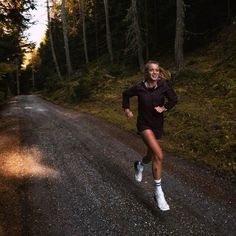 a woman running down a dirt road in the woods