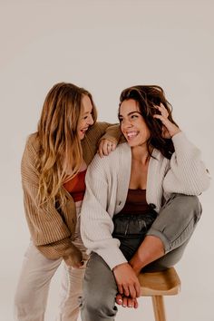 two young women sitting on top of a stool smiling at each other while they both have their arms around one another