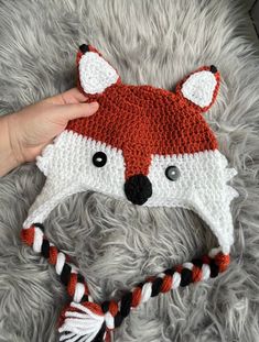 a crocheted hat with a fox design on it and a person's hand next to it