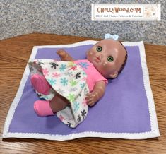 a baby doll laying on top of a purple and white blanket next to a wooden table