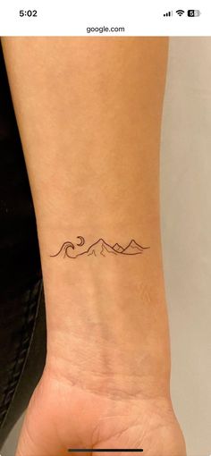 a woman's wrist tattoo with mountains in the distance on her left arm and an arrow