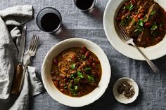 two bowls filled with stew on top of a table next to silverware and spoons