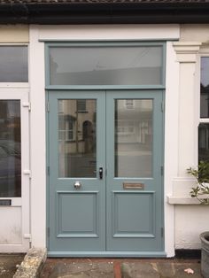 the front door of a building with two windows and a potted plant on the sidewalk