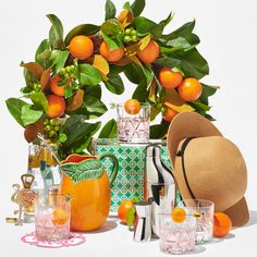 an assortment of oranges and glasses are arranged on a white surface with green leaves