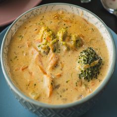 a bowl of broccoli and cheese soup on a blue place mat next to silverware