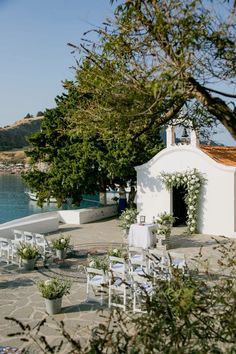 an outdoor wedding setup with white chairs and greenery on the ground next to water