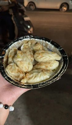 a hand holding a bowl filled with food on top of a table next to parked cars