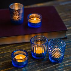 three blue glass votives sitting on top of a table next to a book