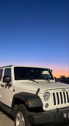 a white jeep is parked in a parking lot at dusk with the sun setting behind it