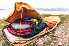 an open sleeping bag sitting on top of a field next to a body of water