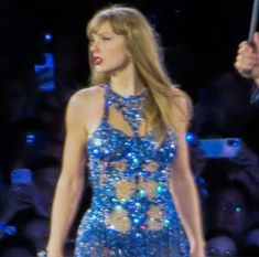 a woman in a blue dress is holding an umbrella and singing on stage with people behind her