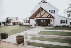 a large white barn with two wooden barrels in front of it and grass on the ground