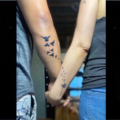 two people holding hands with tattoos on their arms and one has a bird flying above them