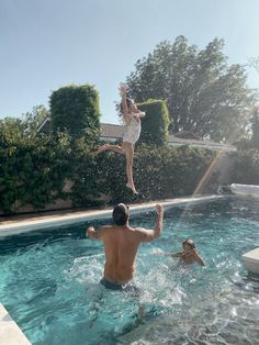 two people jumping into a swimming pool while another person plays in the water behind them