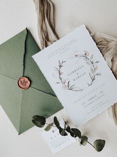 an envelope with a wax stamp on it next to a wedding card and some greenery