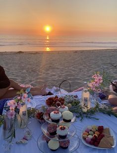 two people sitting at a table with cupcakes and cakes in front of the ocean