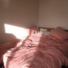 an unmade bed sitting in a bedroom next to a window with the sun shining on it