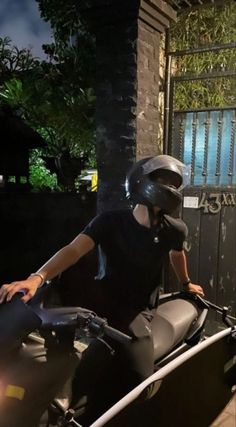 a man riding on the back of a motorcycle next to a gate at night time