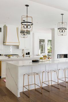 a kitchen with white cabinets and marble counter tops, gold accents on the bar stools