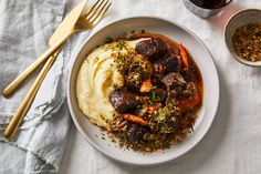 a white plate topped with meat and mashed potatoes next to a glass of wine