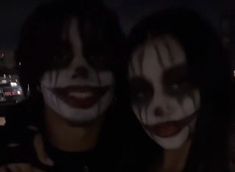 two people with painted faces pose for a photo together at night in front of the city lights