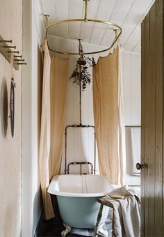 an old fashioned claw foot bathtub in the corner of a bathroom with curtains hanging over it