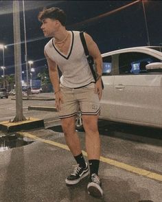 a man standing in the middle of a street next to a white car at night