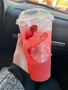 a person holding up a cup with strawberries on it in the backseat of a car