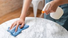 a person wiping down a marble table with a micro towel and spray bottle on it