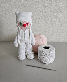 a crocheted cat sitting next to two balls of yarn and a ball of knitting needles